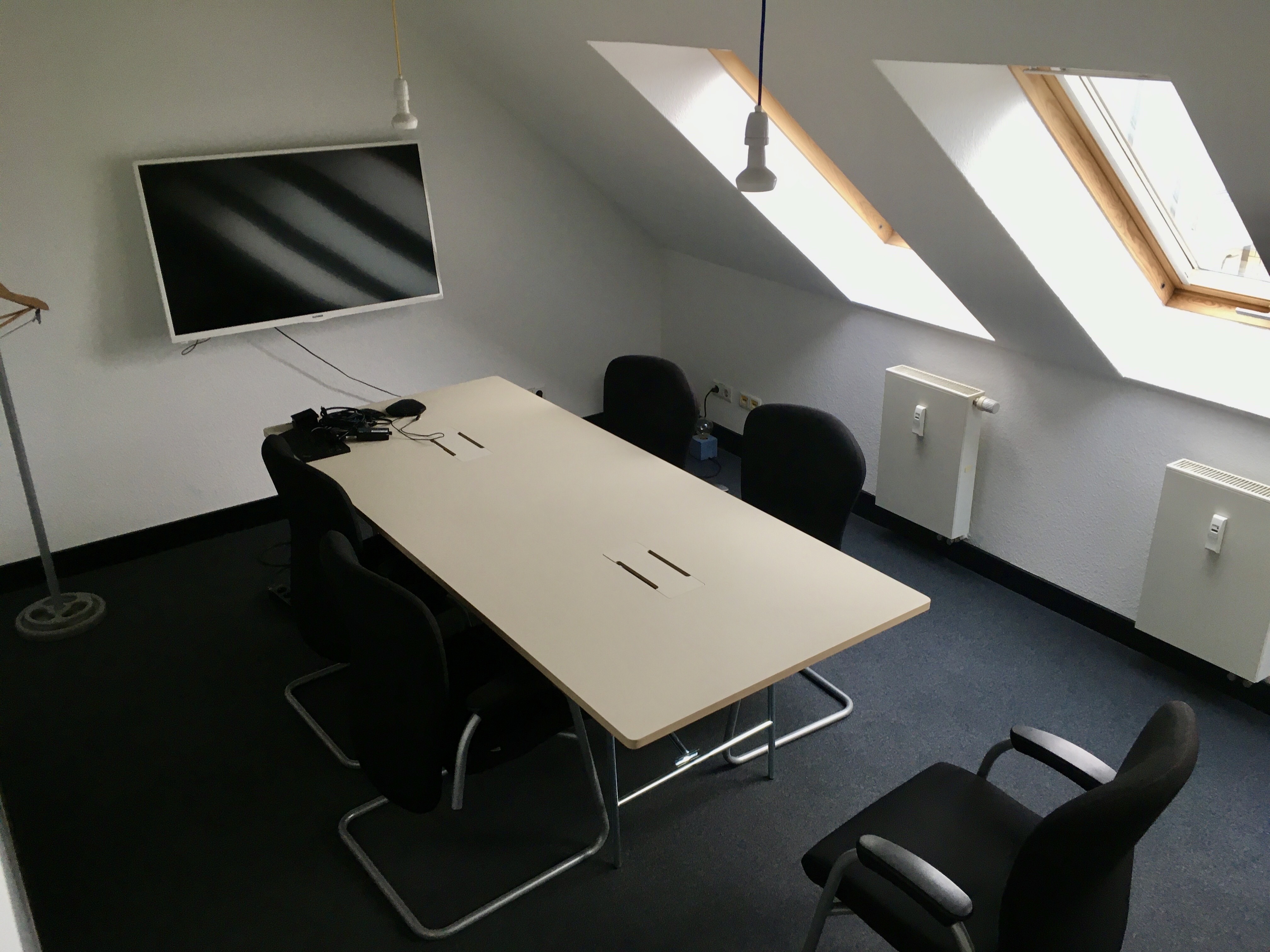 ein raum mit blauen teppich, in der mitte steht ein tisch und an die wand hängt ein fernseher