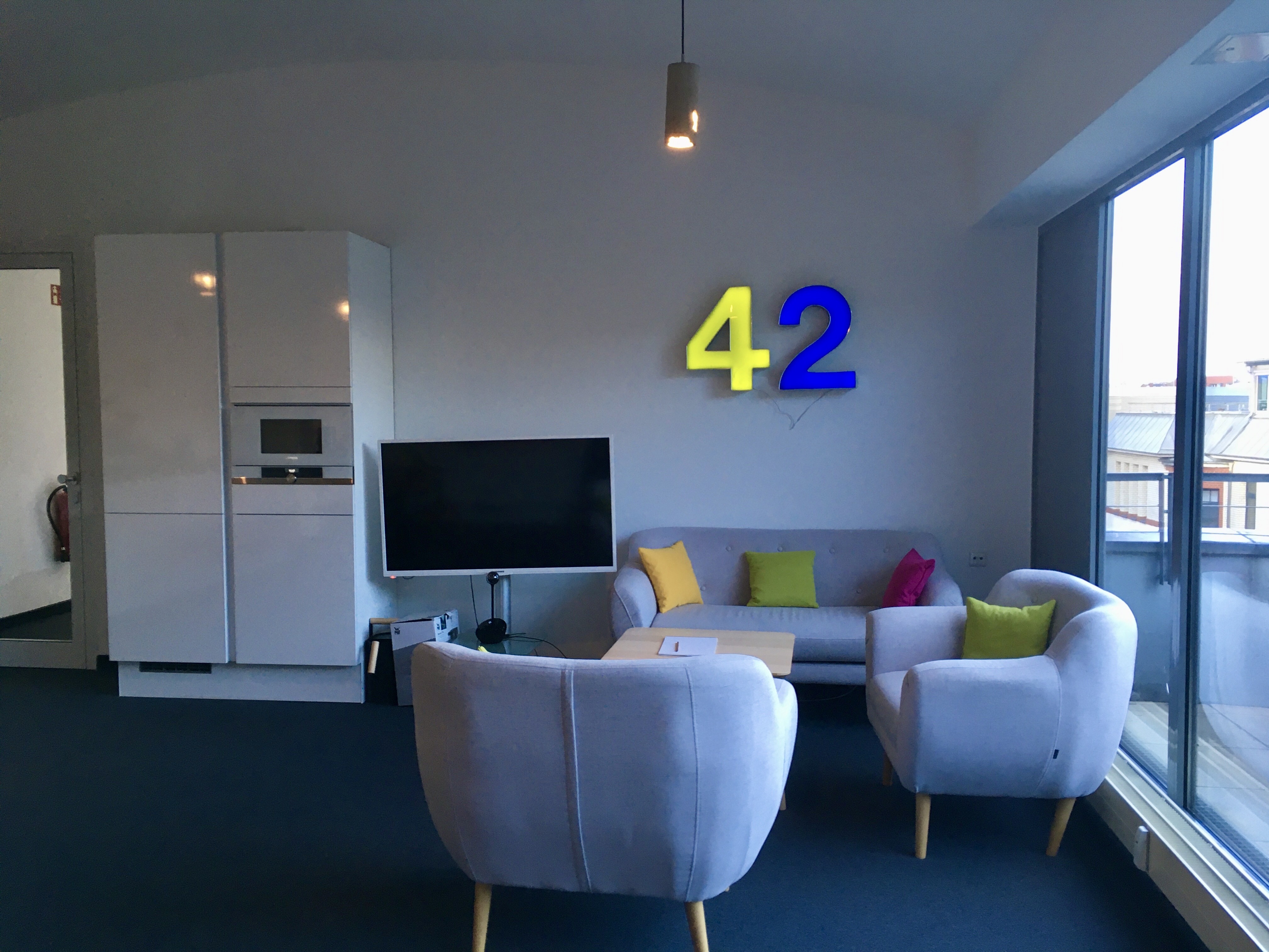 Zwei Sesseln und eine Sofa die einander zugewandt sind. neben den Sofa befindet sich ein Fernseher und ein Kühlschrank. 