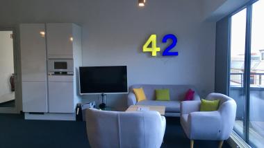 Zwei Sesseln und eine Sofa die einander zugewandt sind. neben den Sofa befindet sich ein Fernseher und ein Kühlschrank.